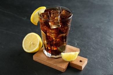 Glass of refreshing soda water with ice cubes and lemon on black table