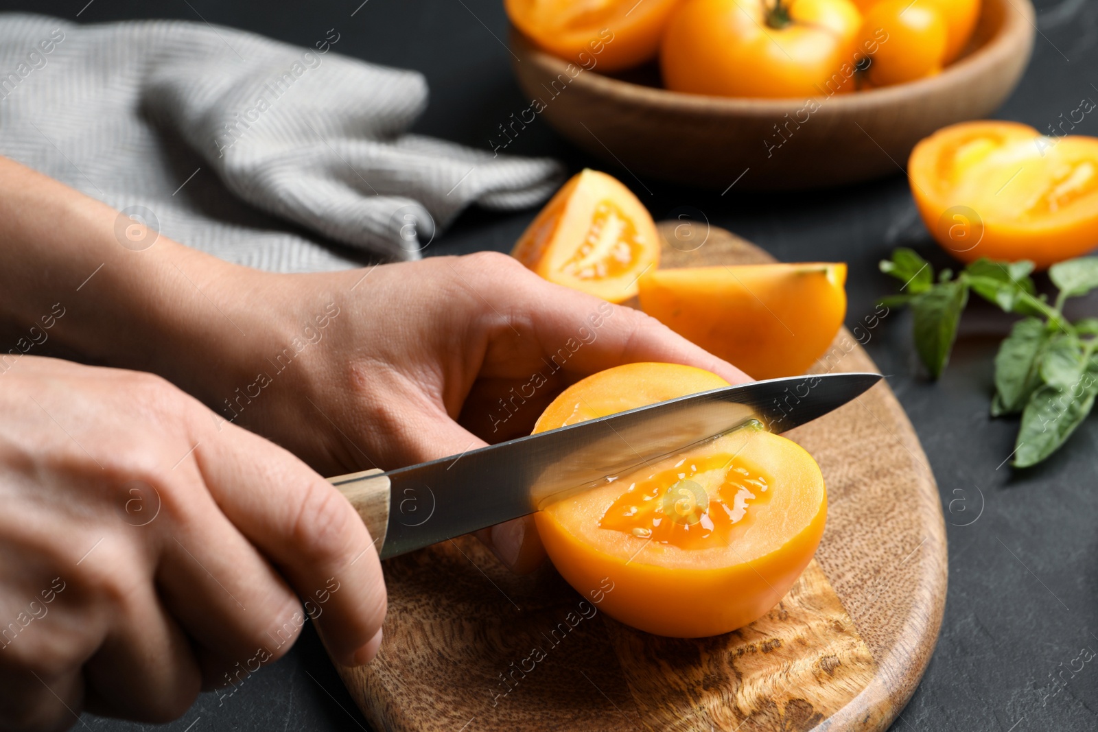 Photo of Woman cutting fresh ripe yellow tomato at black table, closeup