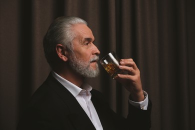 Senior man in suit drinking whiskey on brown background