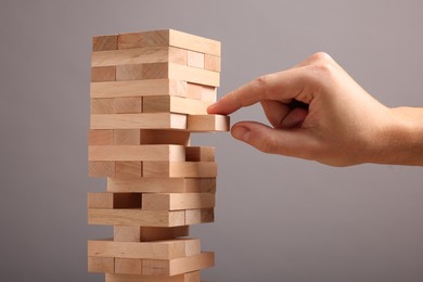 Photo of Playing Jenga. Man removing wooden block from tower on grey background, closeup