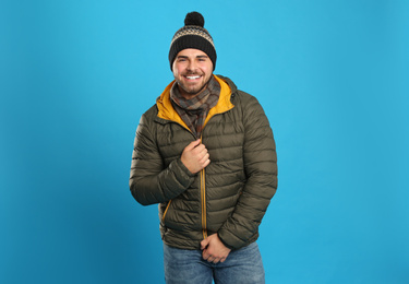 Photo of Happy young man in warm clothes on blue background. Winter vacation
