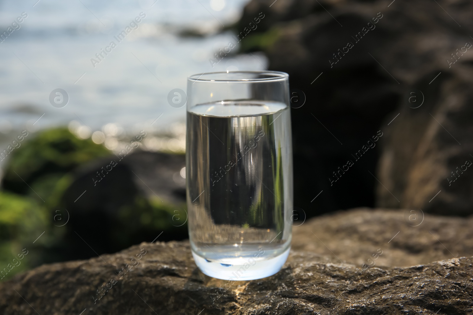 Photo of Glass of fresh water on stone near sea