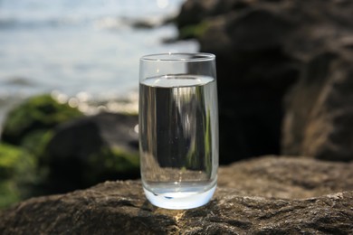 Glass of fresh water on stone near sea