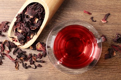 Photo of Cup of fresh hibiscus tea and dry flower leaves on wooden table, flat lay