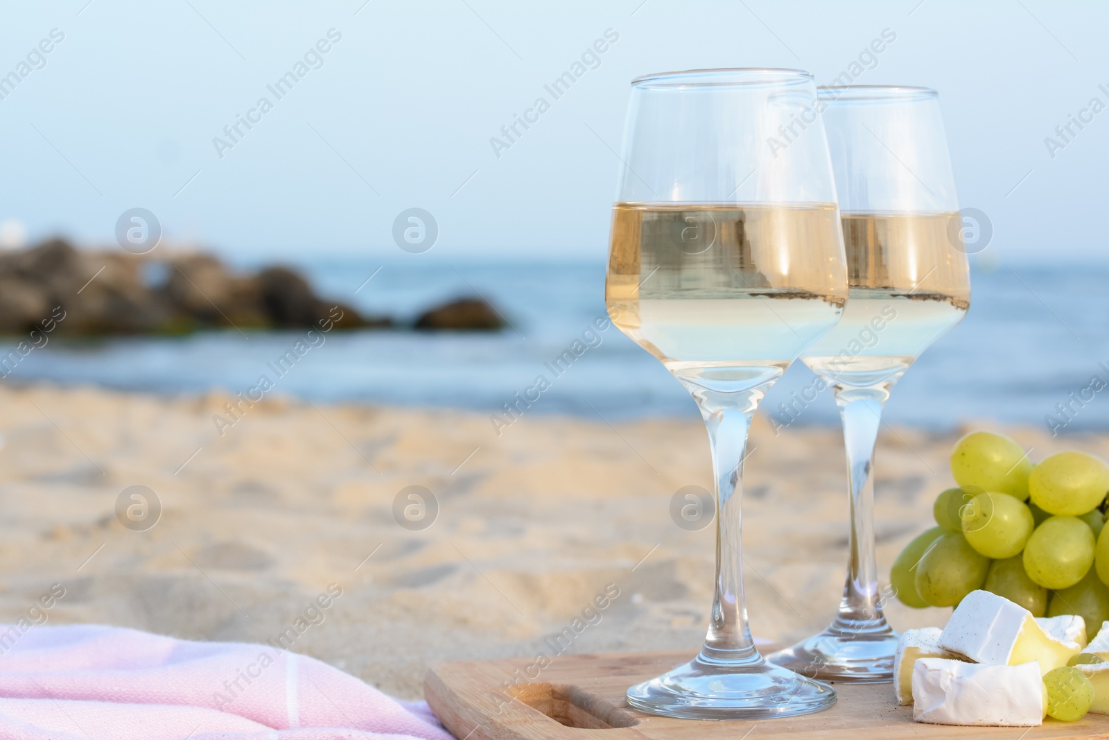 Photo of Glasses with white wine and snacks on sandy seashore. Space for text