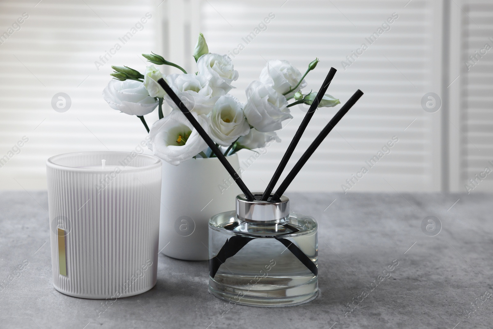 Photo of Reed diffuser, scented candle and eustoma flowers on gray marble table