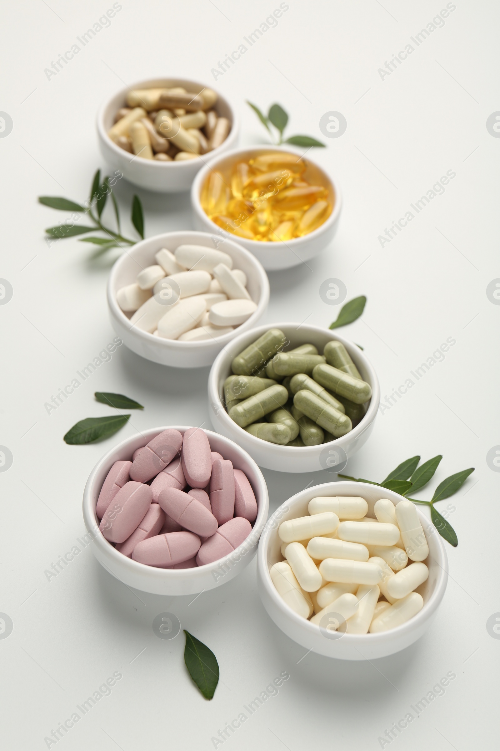 Photo of Different vitamin capsules in bowls and leaves on white background