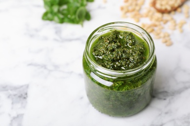 Photo of Homemade basil pesto sauce in glass jar on table