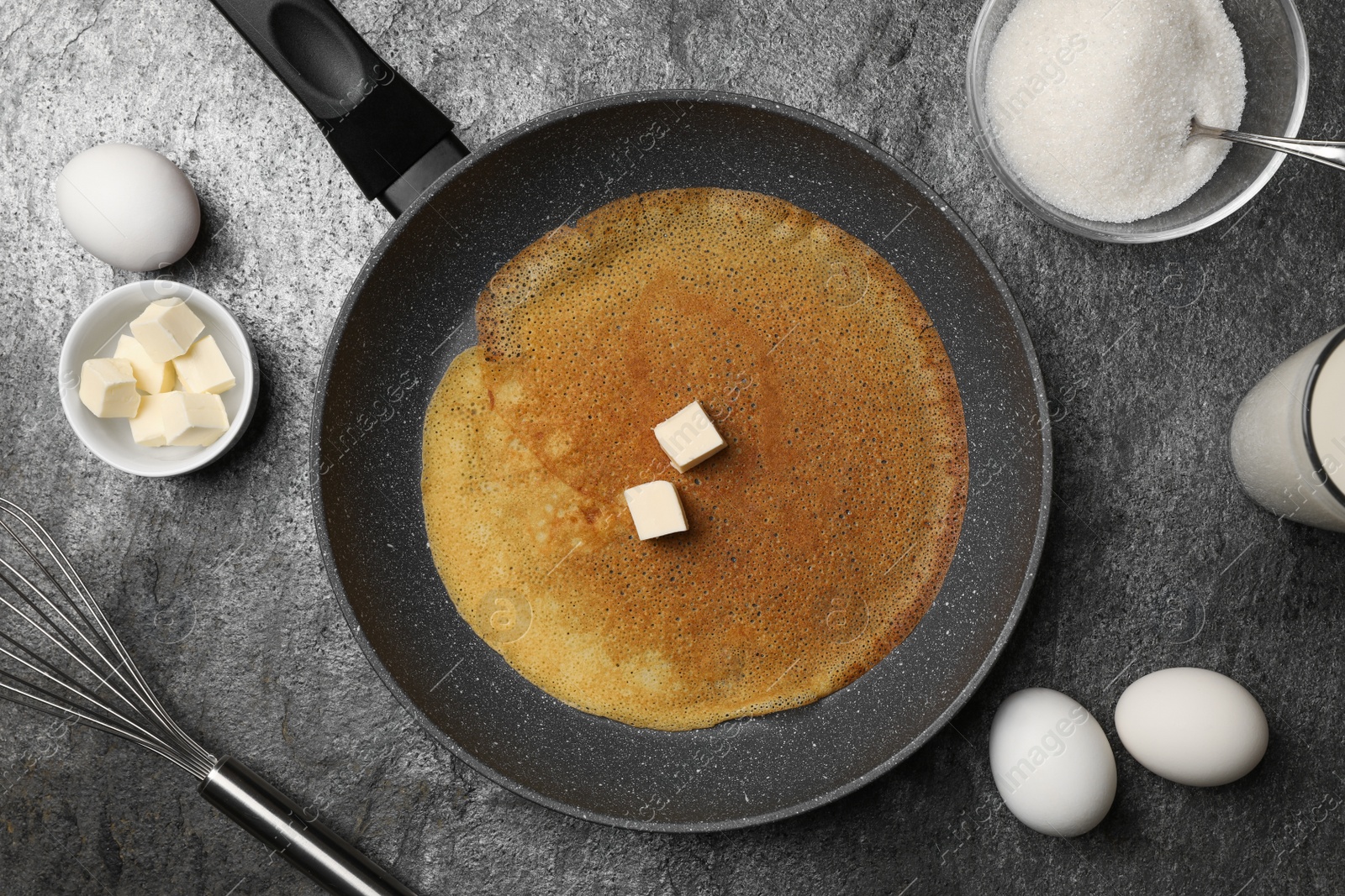 Photo of Frying pan with delicious crepe and ingredients on grey table, flat lay