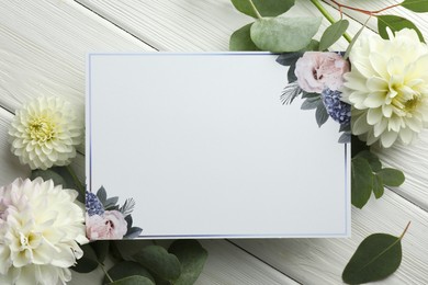 Photo of Blank invitation card and beautiful flowers on white wooden background, flat lay. Space for text