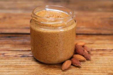 Photo of Tasty nut paste in jar and almonds on wooden table, closeup