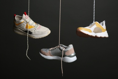 Photo of Different sneakers hanging on black background. Stylish shoes