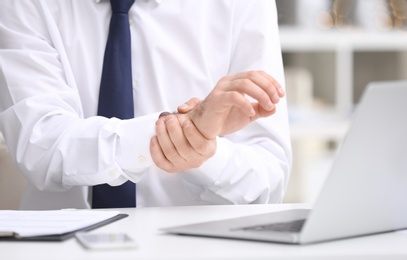 Photo of Young man suffering from wrist pain in office