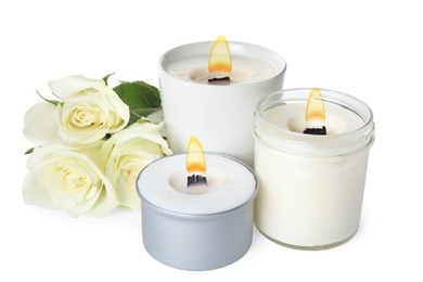 Aromatic candles with wooden wicks and beautiful flowers on white background