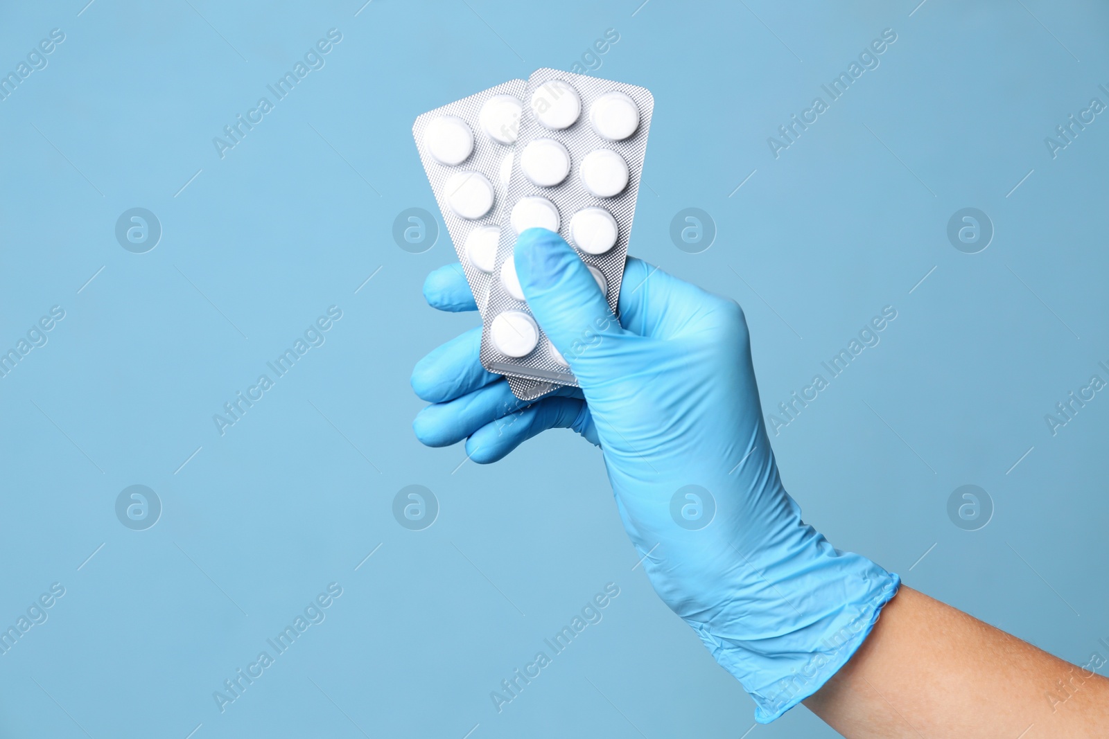 Photo of Scientist in protective gloves holding pills on light blue background, closeup