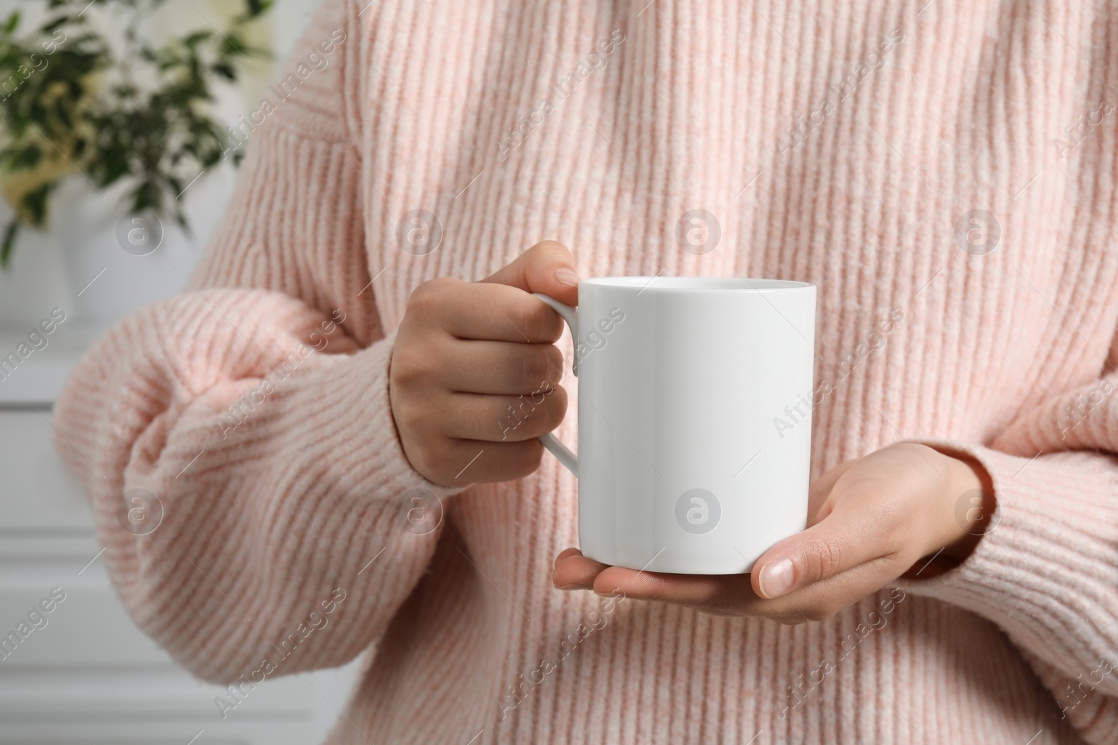 Photo of Woman holding white mug at home, closeup. Mockup for design