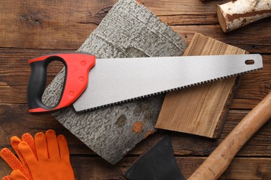 Photo of Saw with colorful handle, axe and logs on wooden background, flat lay