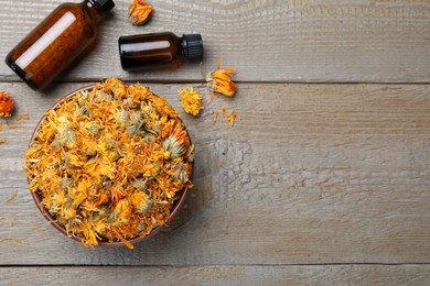 Dry calendula flowers and bottles with tincture on wooden table, flat lay. Space for text