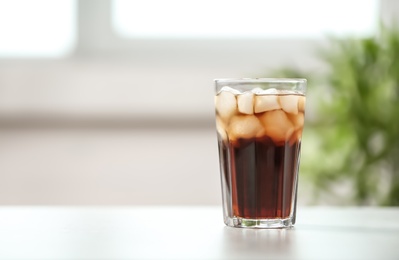 Glass of cola with ice on table against blurred background, space for text