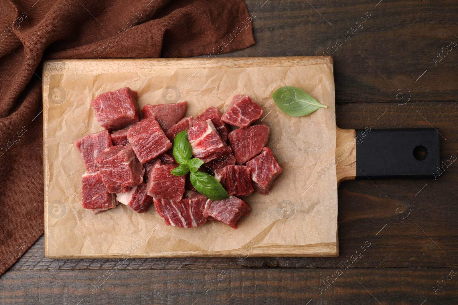 Photo of Cut fresh beef meat with basil leaves on wooden table, top view