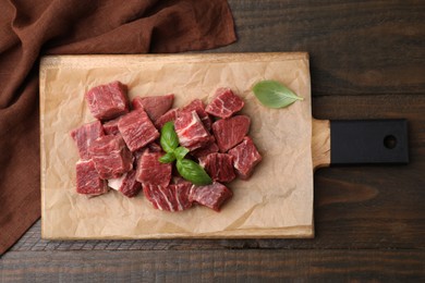 Photo of Cut fresh beef meat with basil leaves on wooden table, top view