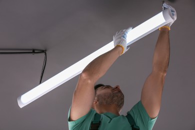 Photo of Ceiling light. Electrician installing led linear lamp indoors, low angle view