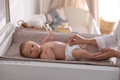 Mother changing her baby's diaper on table in room