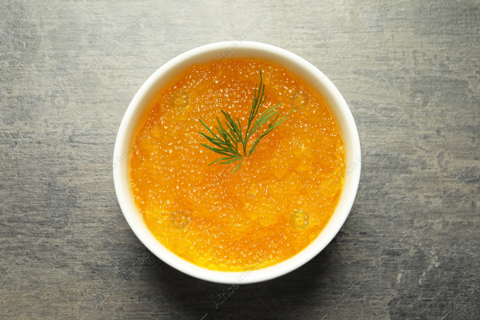 Photo of Fresh pike caviar and dill in bowl on grey table, top view