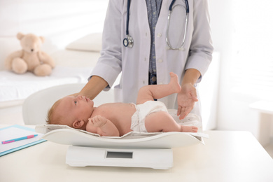 Doctor weighting cute baby in clinic, closeup. Health care