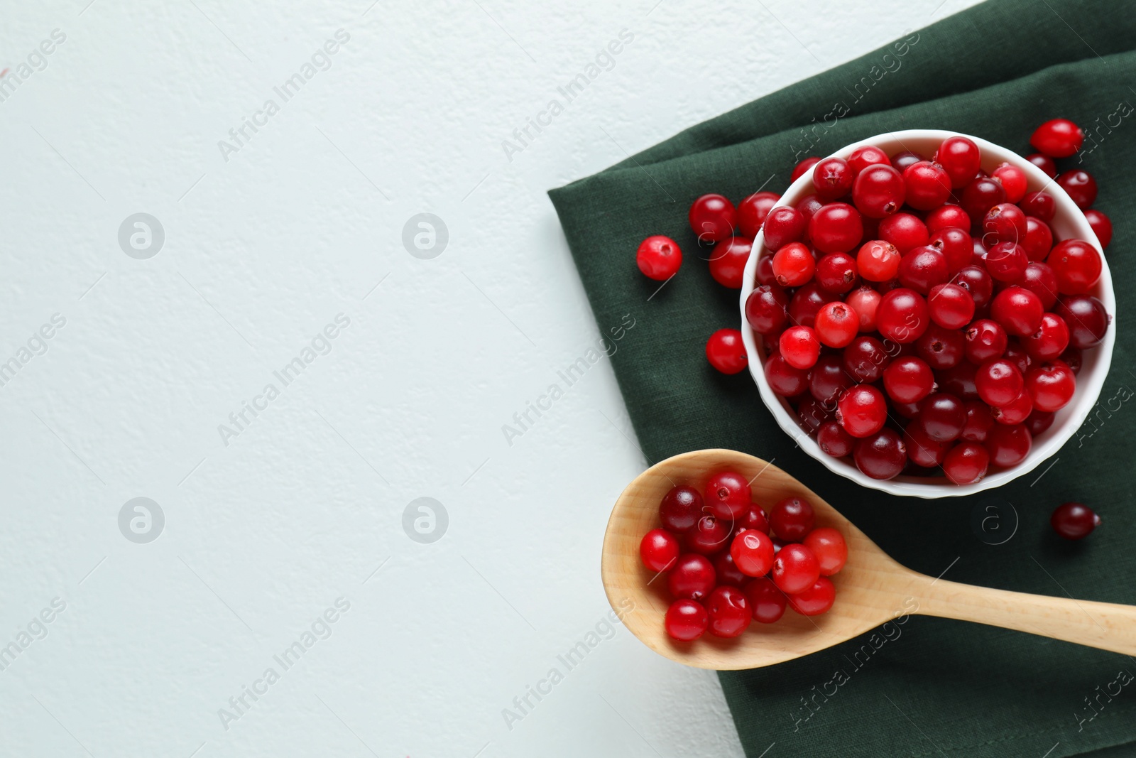 Photo of Cranberries in bowl and spoon on white table, top view. Space for text