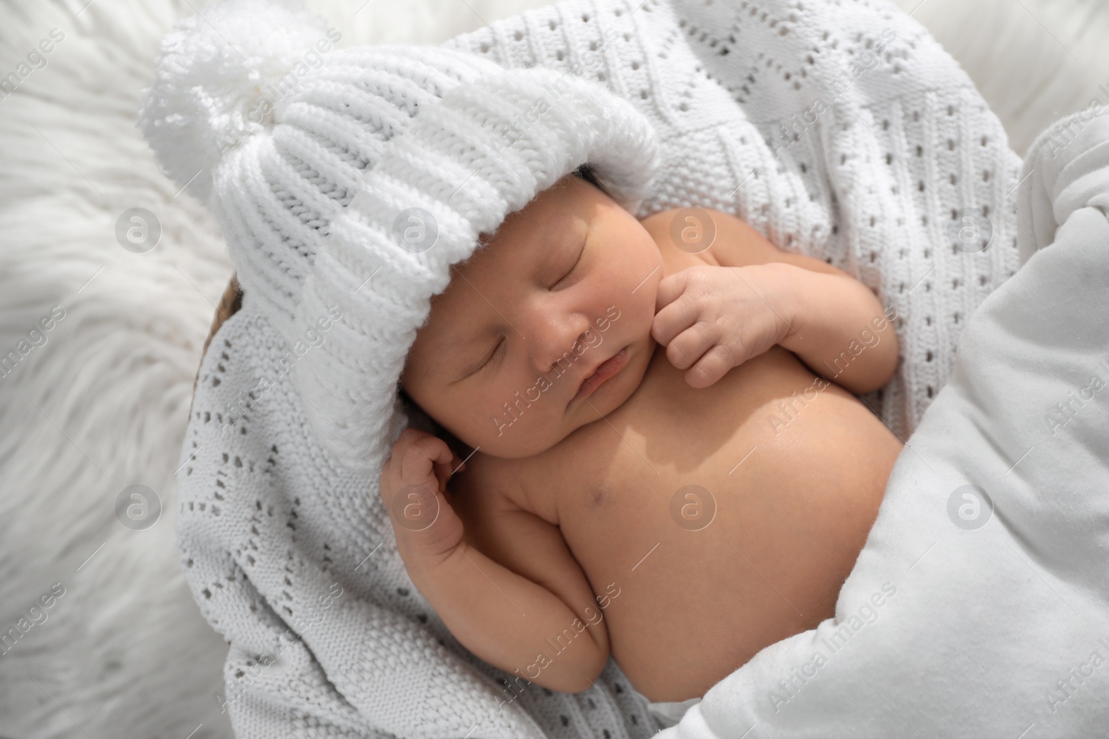 Photo of Cute newborn baby in warm hat sleeping on knitted blanket, top view