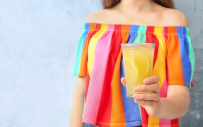 Young woman with glass of lemon juice on color background, closeup