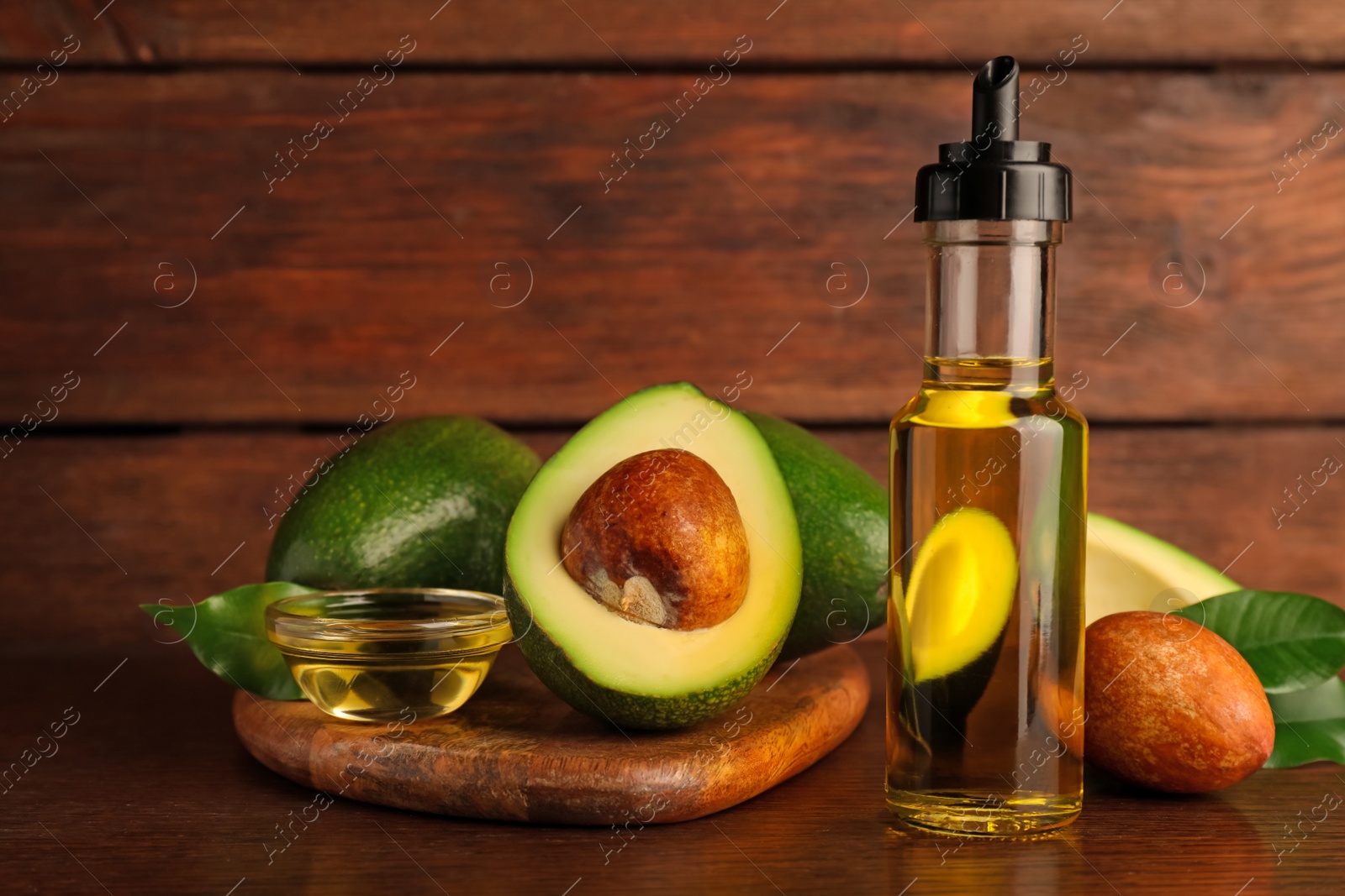 Photo of Glass bottle of cooking oil and fresh avocados on wooden table