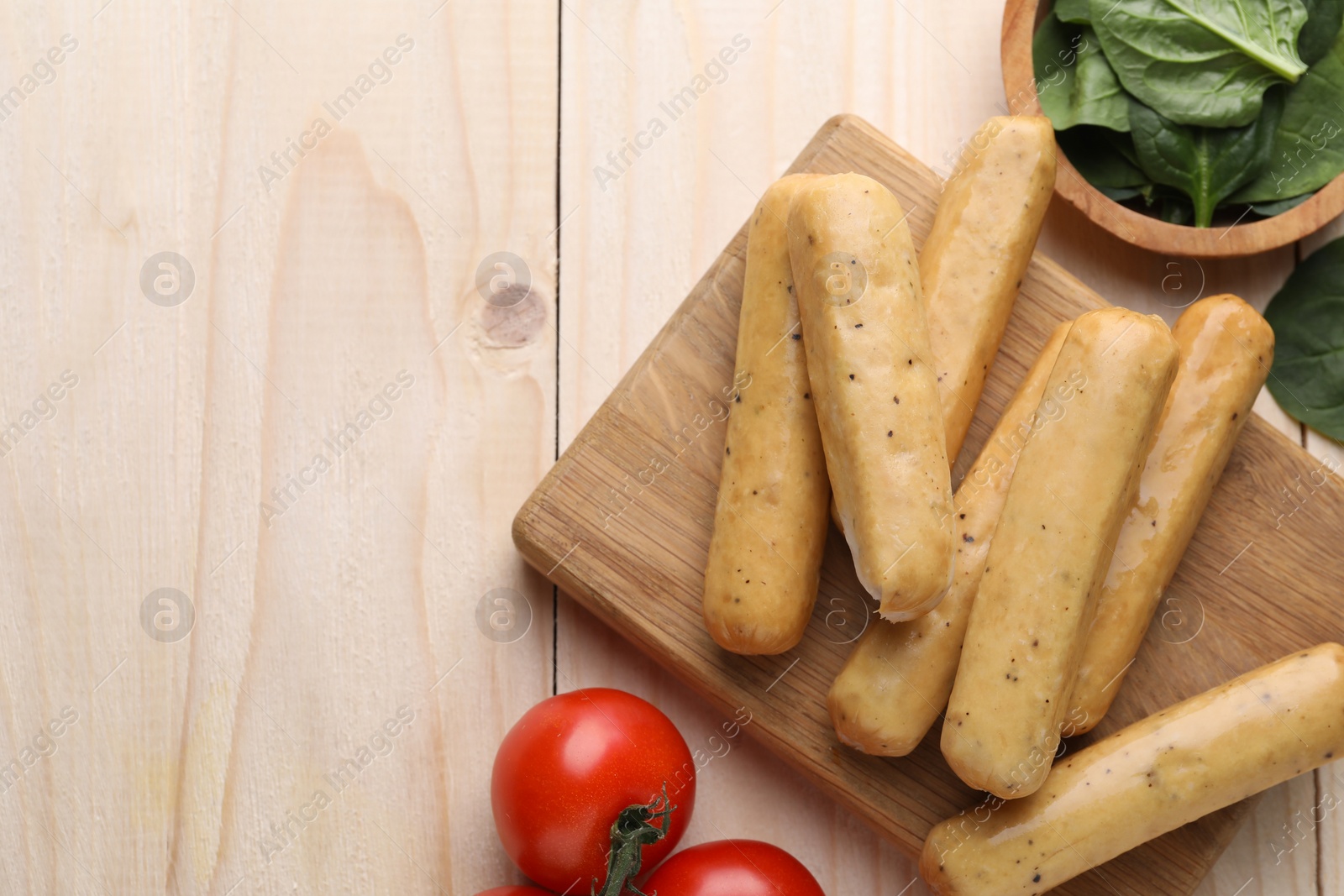 Photo of Raw vegan sausages with tomatoes and spinach on wooden table, flat lay. Space for text