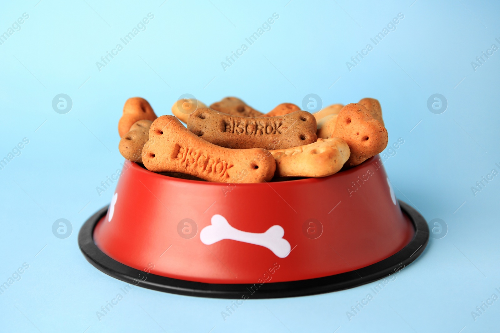 Photo of Bone shaped dog cookies in feeding bowl on light blue background