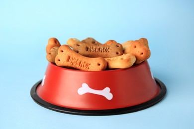 Bone shaped dog cookies in feeding bowl on light blue background