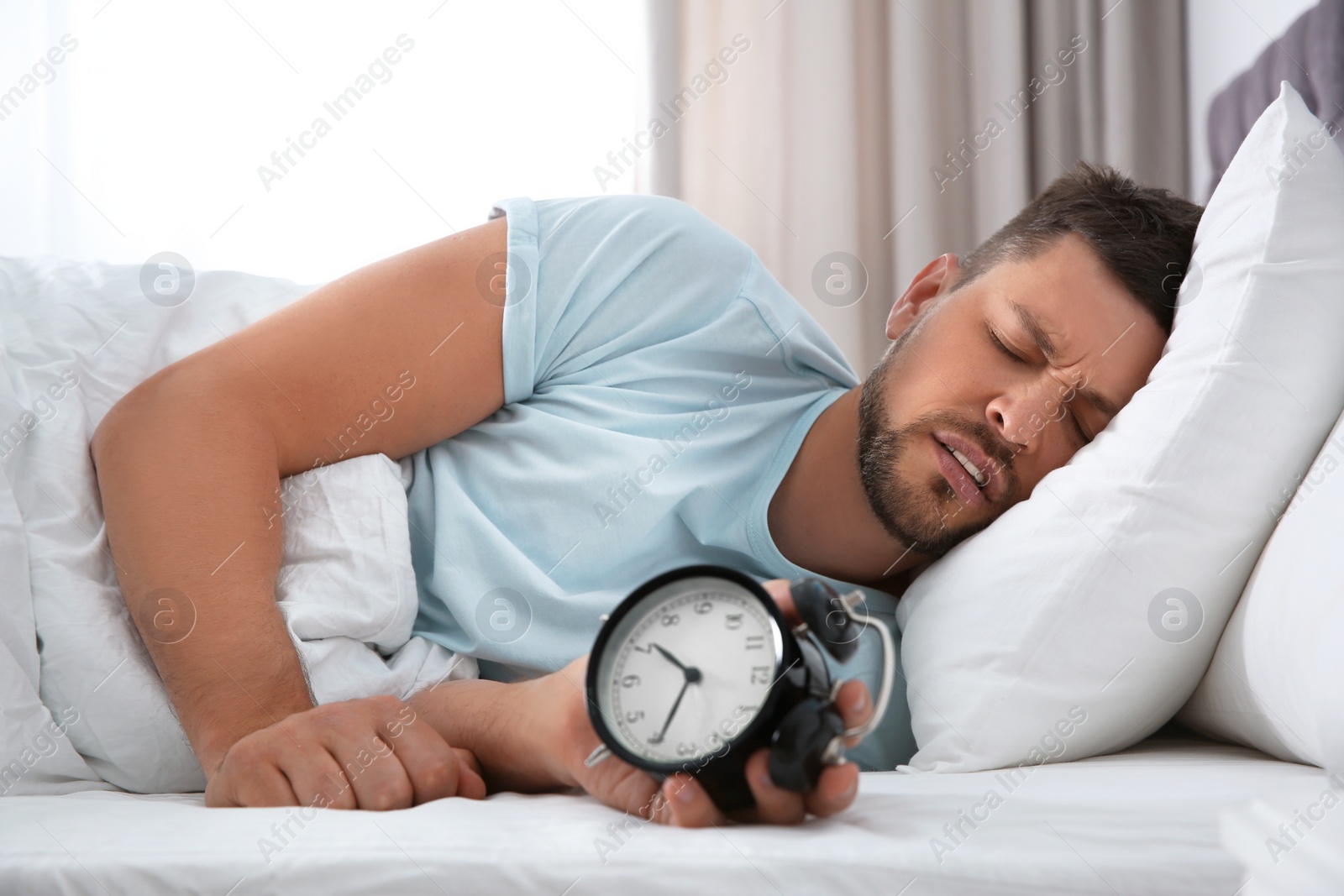 Photo of Sleepy man with alarm clock at home in morning