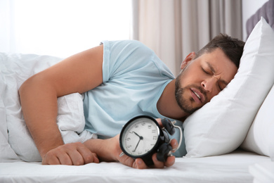 Sleepy man with alarm clock at home in morning