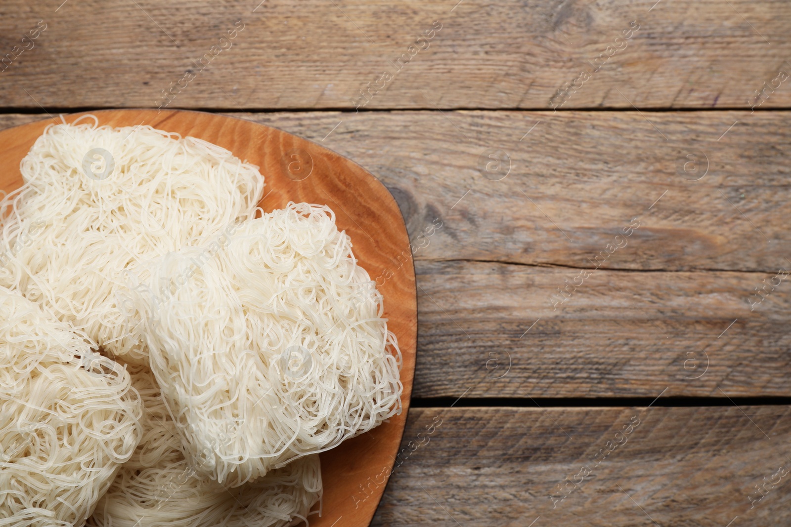 Photo of Plate with uncooked rice noodles on wooden table, top view. Space for text