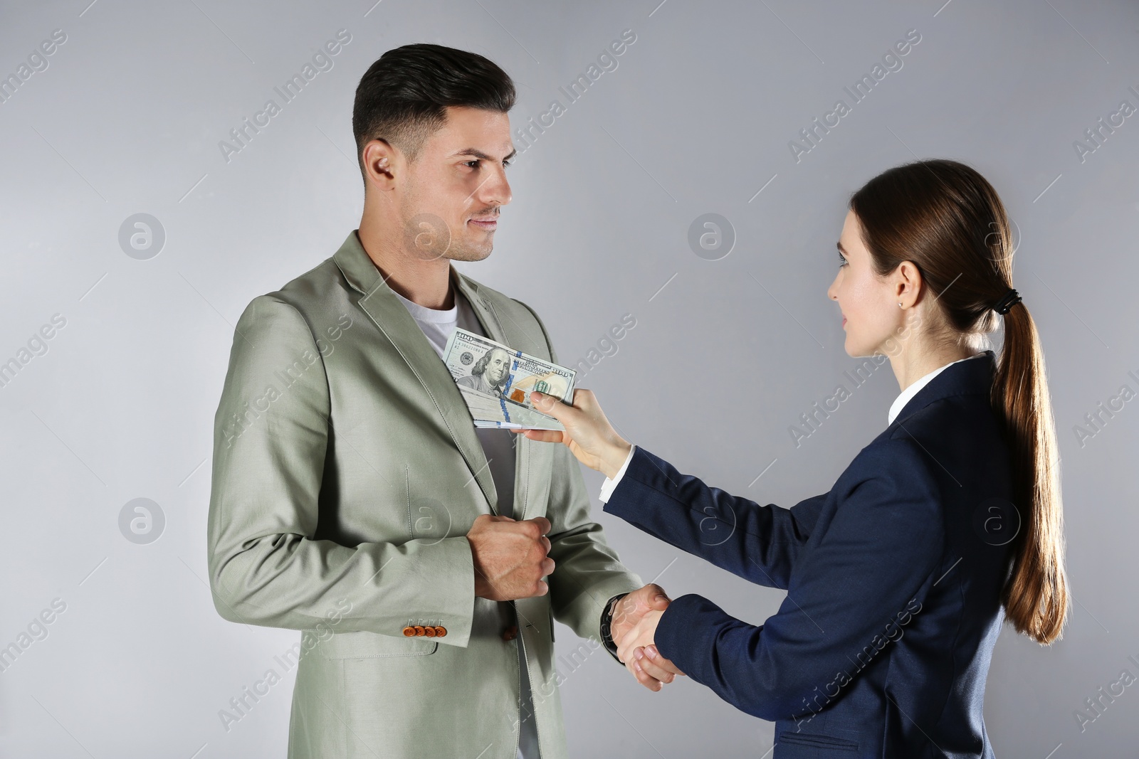 Photo of Woman shaking hands with man and offering bribe on grey background