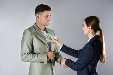 Photo of Woman shaking hands with man and offering bribe on grey background