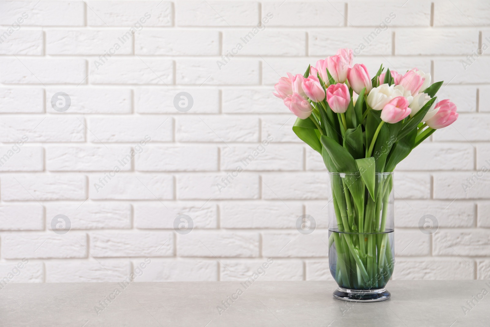 Photo of Beautiful bouquet of tulips in glass vase on light table. Space for text