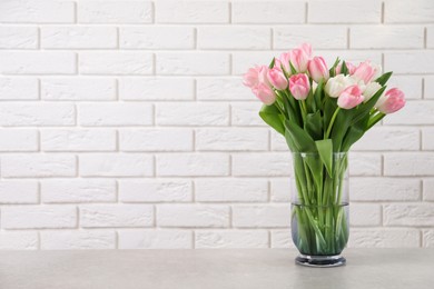 Beautiful bouquet of tulips in glass vase on light table. Space for text