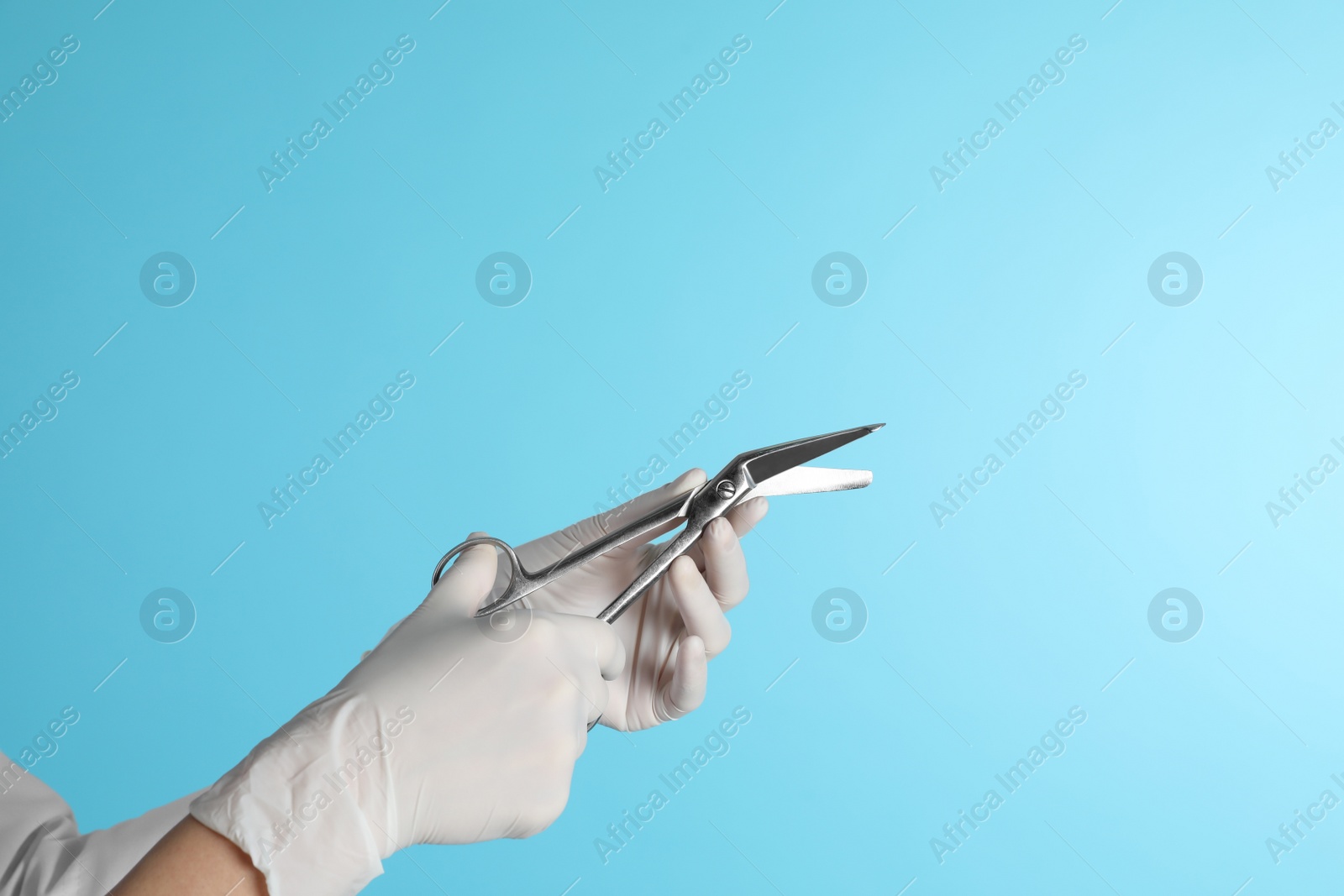 Photo of Female doctor holding bandage scissors on color background, closeup view with space for text. Medical object
