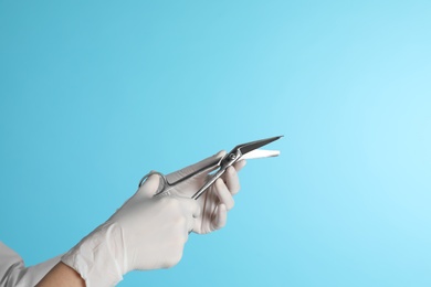 Photo of Female doctor holding bandage scissors on color background, closeup view with space for text. Medical object