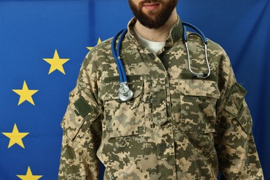 Photo of Man in military uniform with stethoscope against flag of European Union, closeup. Health care concept