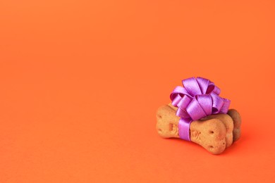 Photo of Bone shaped dog cookies with purple bow on orange background. Space for text
