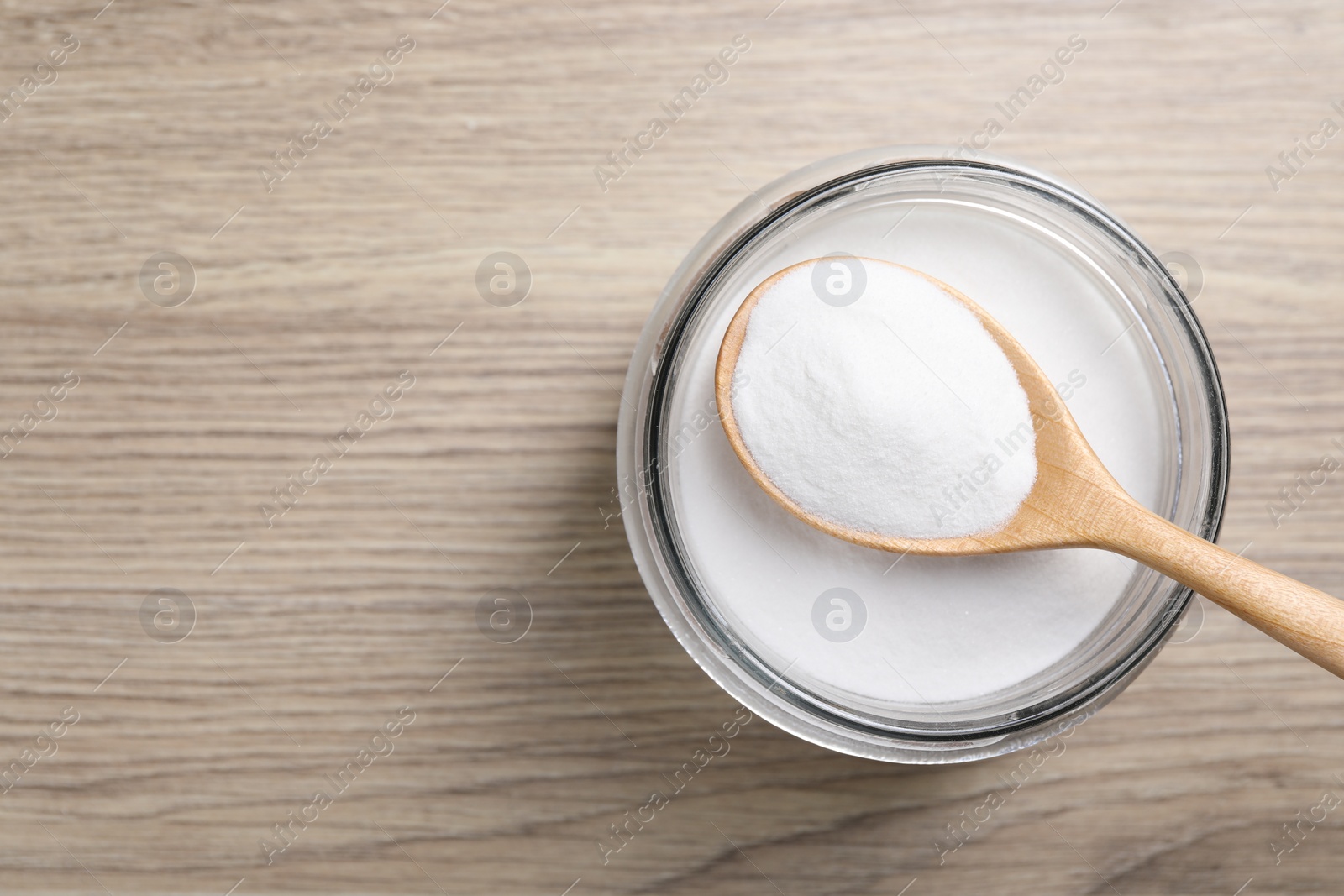 Photo of Baking soda in glass jar on wooden table, top view. Space for text