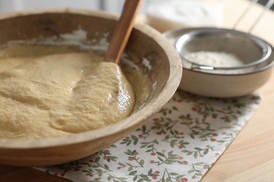 Photo of Raw dough in bowl on wooden table, closeup