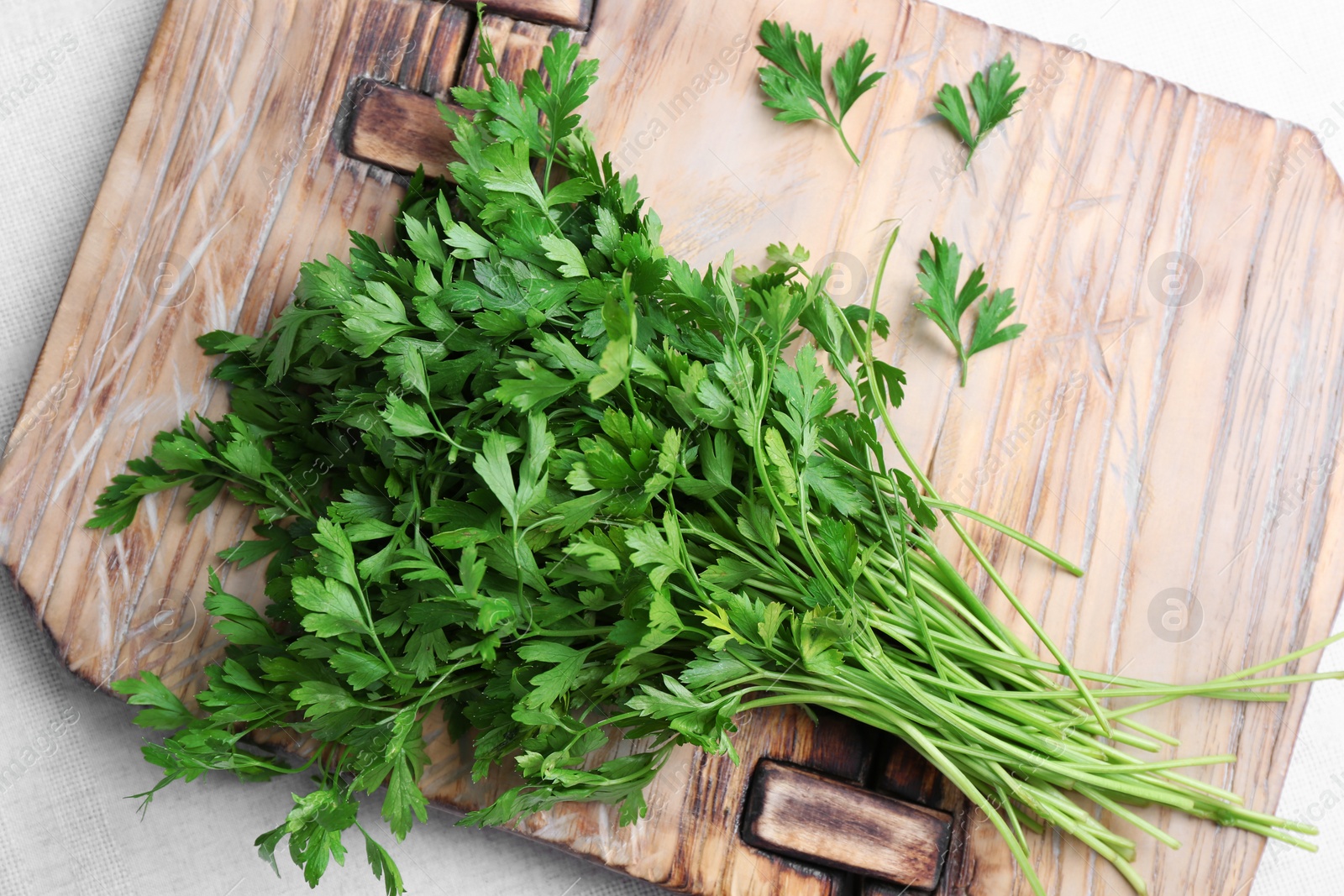 Photo of Wooden board with fresh green parsley on light fabric, top view